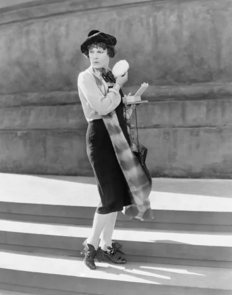 Giovane donna su gradini, tenendo un soffio di polvere — Foto Stock