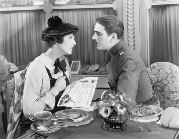 Homem de uniforme e uma mulher sentados juntos em uma mesa e olhando um para o outro — Fotografia de Stock