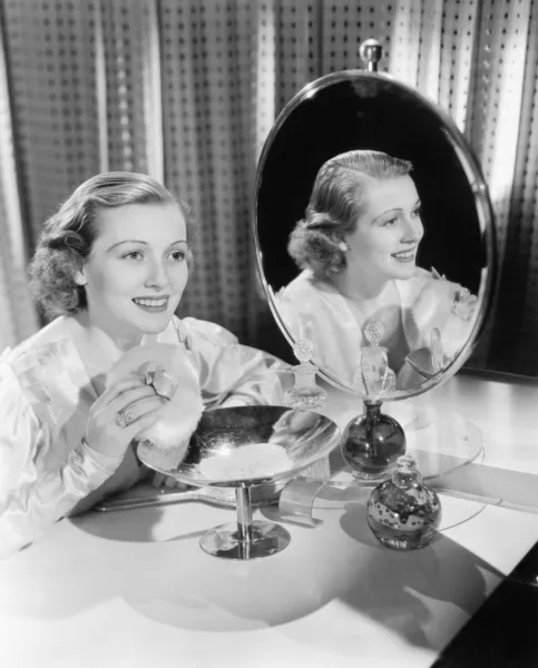 Mujer joven sentada al lado del espejo y sosteniendo una bocanada de polvo —  Fotos de Stock