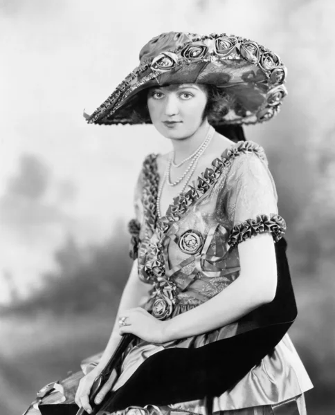 Uma jovem elegante com um chapéu grande e um lindo vestido ornamentado — Fotografia de Stock