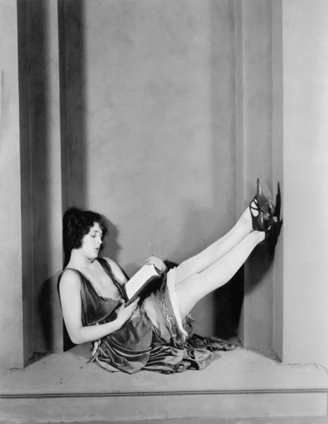 Junge Frau sitzt mit erhobenen Beinen und liest — Stockfoto