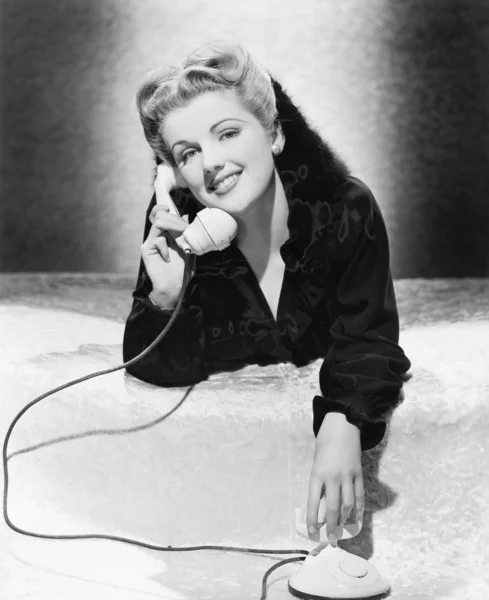 Mujer joven acostada boca abajo y hablando por teléfono — Foto de Stock