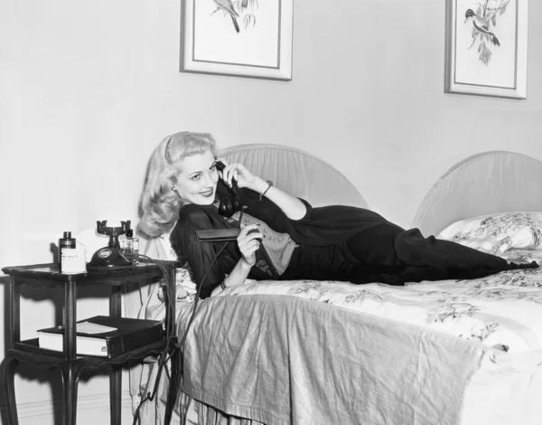 Ung kvinna liggande på hennes säng i sovrummet och pratar i telefon — Stockfoto