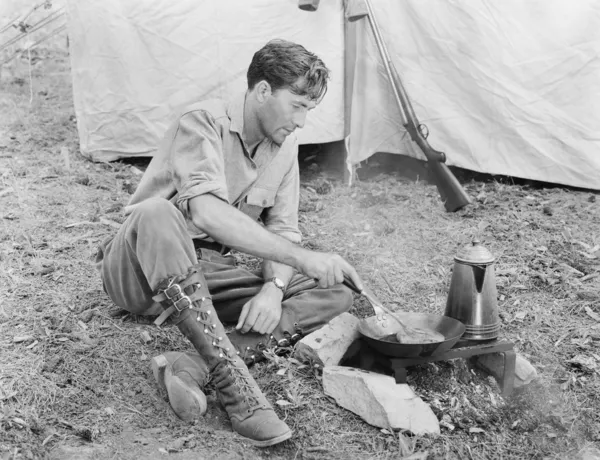 Człowiek siedzi przed jego namiot przygotowywania żywności — Zdjęcie stockowe
