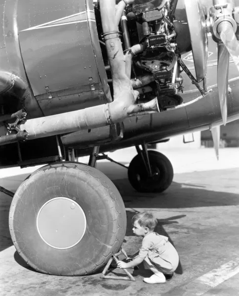 Malý chlapec snaží opravit kolečko letadla — Stock fotografie
