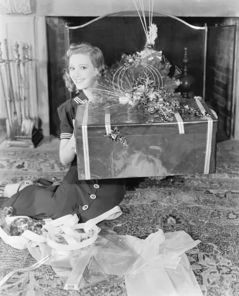 Νεαρή γυναίκα που κάθεται σε ένα καθιστικό που δείχνει ένα δώρο — Φωτογραφία Αρχείου