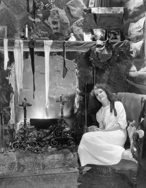 Jovem mulher sentada na frente de uma lareira, secando suas meias — Fotografia de Stock