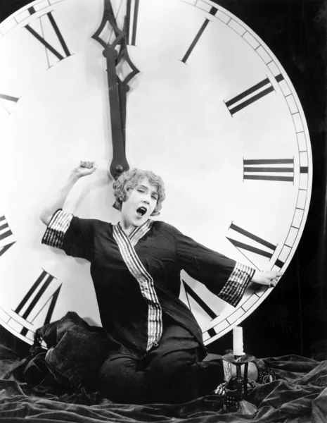 En ung kvinna som sträcker sig framför en gigantisk klocka slående midnatt — Stockfoto