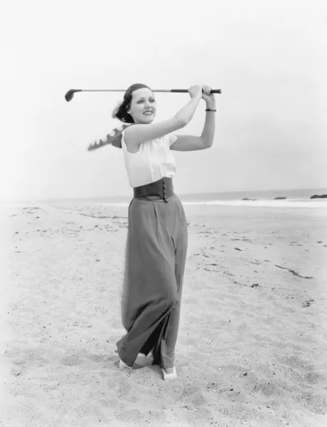Молодая женщина играет в гольф на пляже — стоковое фото