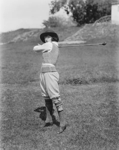 Ung kvinna svinga en golfklubba på en golfbana — Stockfoto