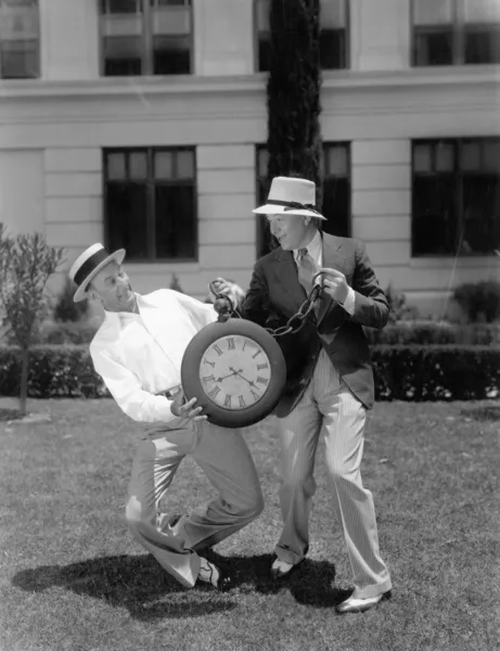 Dos hombres luchando con un reloj de bolsillo de gran tamaño — Foto de Stock