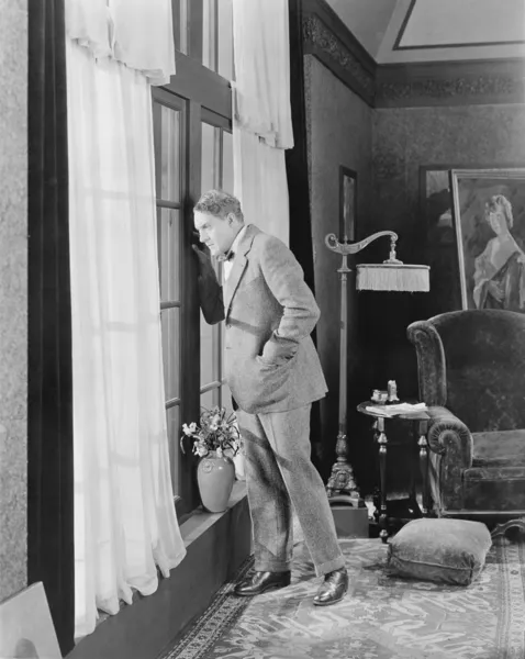 Homem numa sala de estar a olhar pela janela — Fotografia de Stock