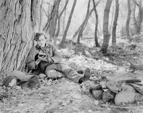 Man sitting next to a fire in the woods and reading a book — Stok fotoğraf