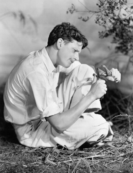 Человек, сидящий снаружи и вырезающий кусок дерева
