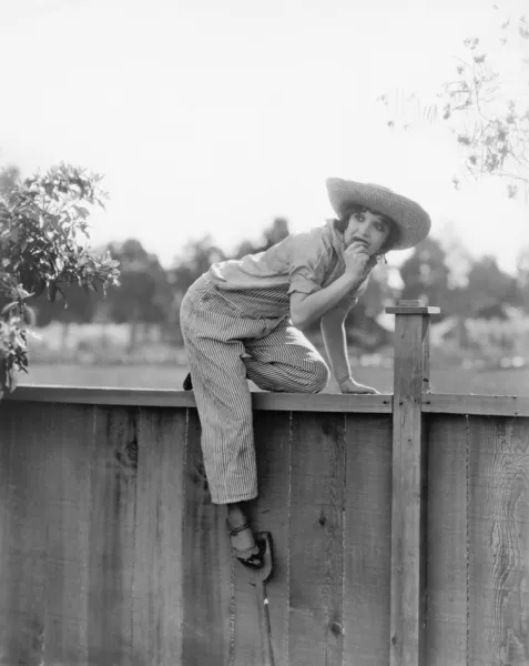 Young woman trying to get over a wooden fence with a fruit in her hands — Stok fotoğraf
