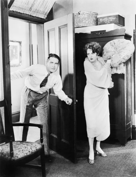 枕を持つ男をヒットしようとすると、ドアの後ろに立っている女性 — ストック写真