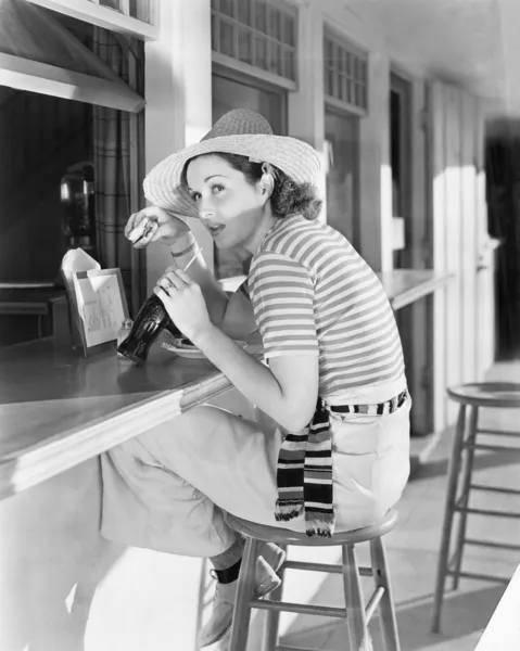 Jovem sentada em um balcão bebendo uma cola de coca — Fotografia de Stock