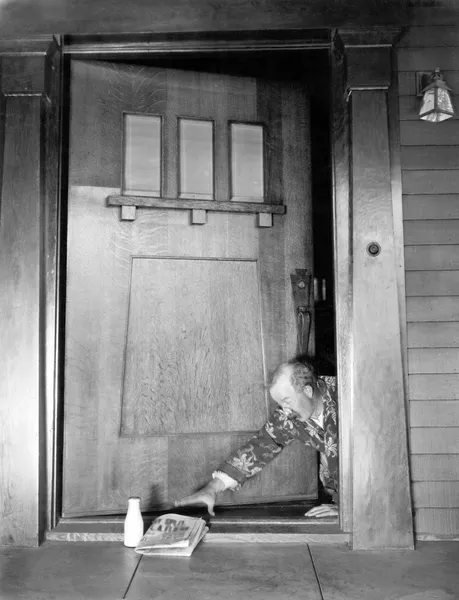 Muž procházení na přední dveře k dosažení své noviny a mléko — Stock fotografie