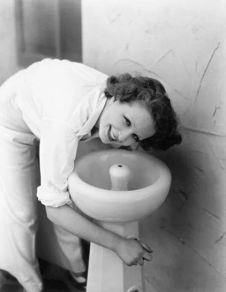 Mujer joven inclinándose sobre una fuente de agua potable — Foto de Stock