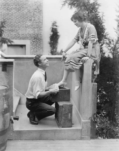 Woman sitting on a ledge having her shoes cleaned by a man — Stock Photo, Image