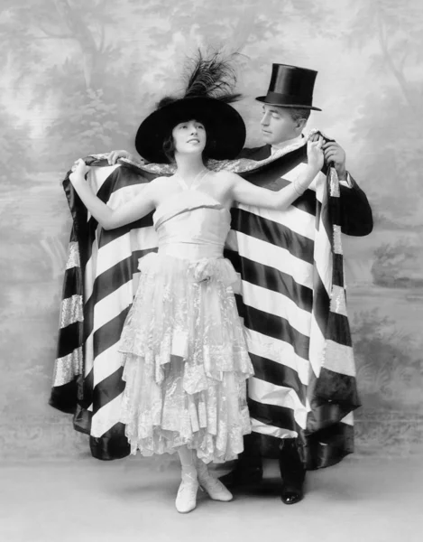 Homme avec un chapeau haut de forme aidant une femme dans une cape — Photo