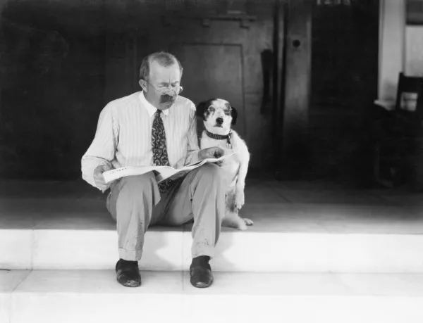 Muž a pes sedí na schodech, čtení novin — Stock fotografie