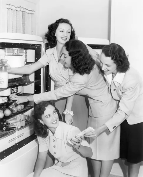 Vier Frauen, die Dinge aus dem Kühlschrank holen — Stockfoto