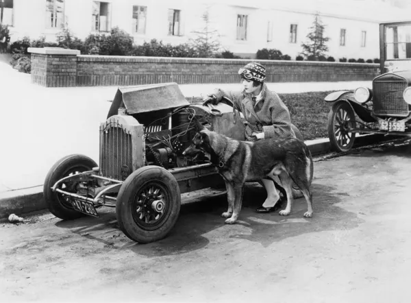 Молодая женщина сидит рядом с маленькой машиной и смотрит на двигатель со своей немецкой овчаркой — стоковое фото