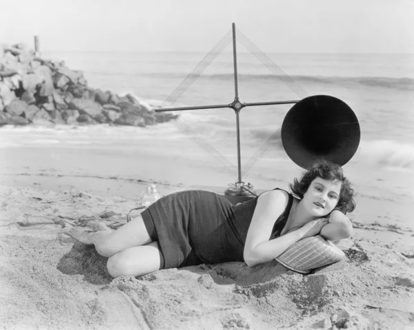 Onun arkasında büyük bir anten ile plajda yatan genç kadın — Stok fotoğraf