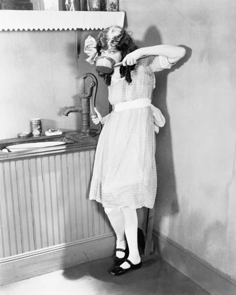 Молодая девушка получает глоток воды из насоса на кухне — стоковое фото