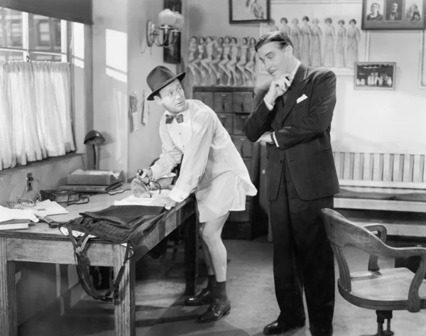 Dos hombres de pie en una oficina, uno planchando sus pantalones — Foto de Stock