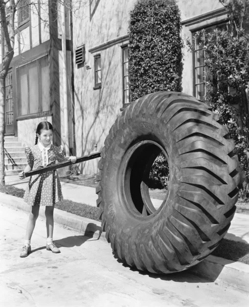Девушка играет с огромной шиной и палкой — стоковое фото