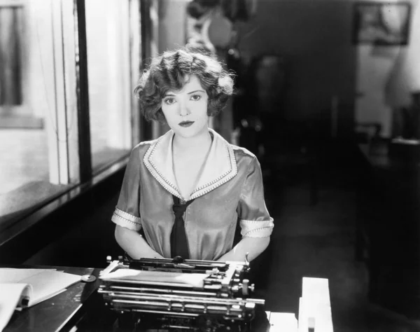 Jovem mulher sentada na frente de uma máquina de escrever — Fotografia de Stock