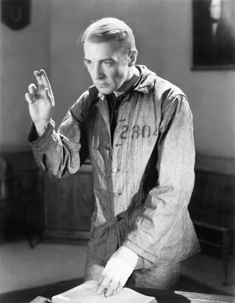 宣誓を誓う彼の指を保持している囚人の服装の男 — ストック写真