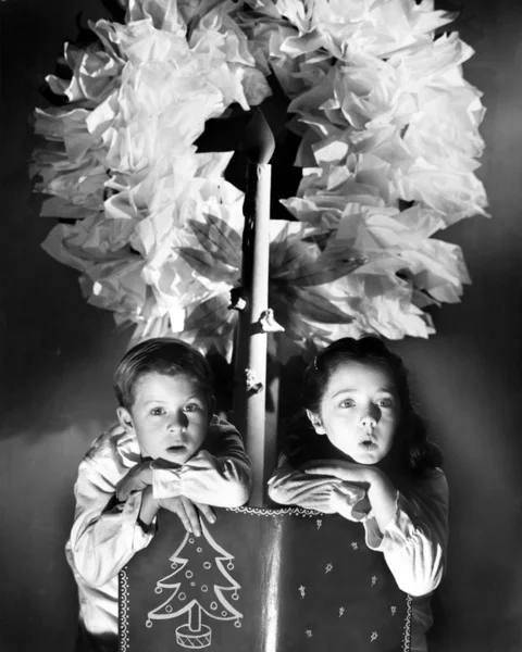 Two children sitting under a wreath holding a Christmas story book — Stock Photo, Image