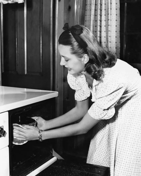 Ung kvinna i hennes kök dra en pott ur ugnen — Stockfoto