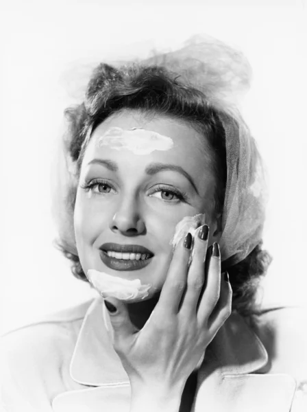 Mujer joven poniendo crema en su cara — Foto de Stock