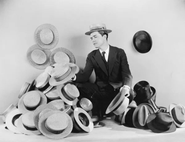 Человек, сидящий на полу в окружении шляп — стоковое фото