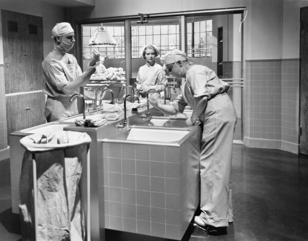 Two surgeons and a nurse in the scrub room preparing for an operation