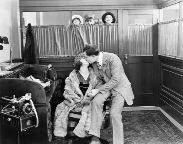 Casal beijando em um escritório, enquanto as crianças e um mensageiro estão espreitando sobre uma cortina — Fotografia de Stock