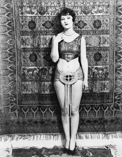Jovem mulher mal vestida na frente de um tapete pendurado — Fotografia de Stock