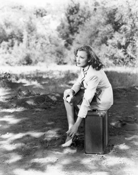 Jovem mulher sentada ao lado da estrada em sua mala, esfregando seus pés doloridos — Fotografia de Stock
