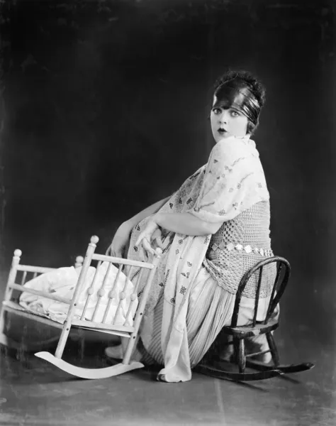 Νεαρή γυναίκα που κάθεται σε μια καρέκλα παιχνίδι δίπλα σε ένα παχνί μωρών παιχνίδι — Φωτογραφία Αρχείου