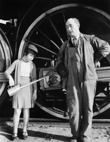 Bambina con una tanica d'olio in piedi accanto a una locomotiva e al macchinista — Foto Stock