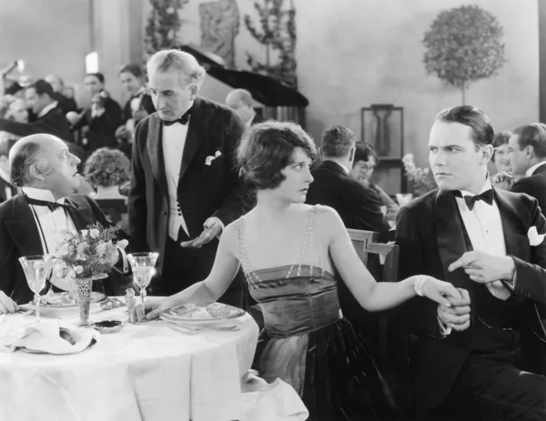 Giovane donna che tiene la mano di un uomo a un tavolo diverso mentre la sua compagna sta parlando con il cameriere — Foto Stock