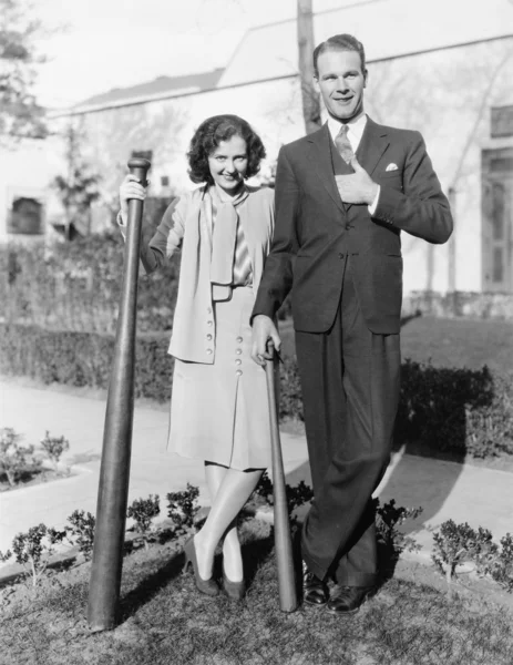 Casal em pé junto com um taco de beisebol de grandes dimensões — Fotografia de Stock