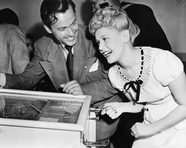 Casal se divertindo e rindo ao lado de uma máquina de pinball — Fotografia de Stock
