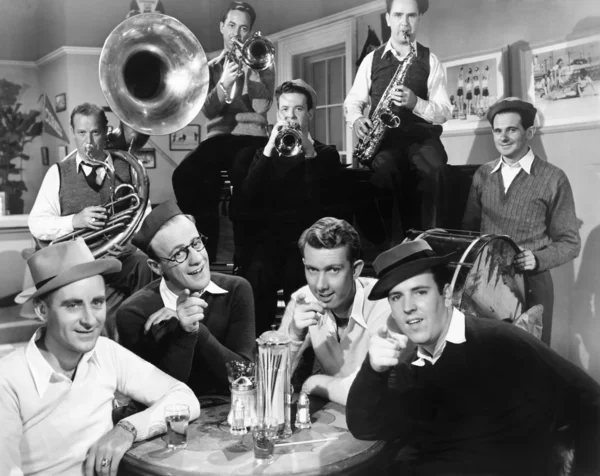 Группа мужчин сидит в закусочной с музыкантами позади них — стоковое фото