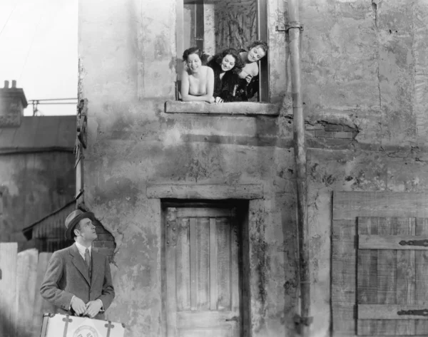 Три жінки, які виглядають з вікна біля чоловіка, що стоїть на вулиці з валізою — стокове фото