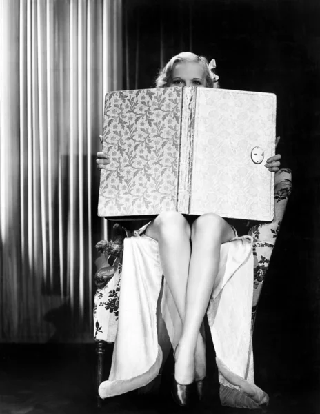 Jonge vrouw op zoek over bovenkant van een oversized boek — Stockfoto